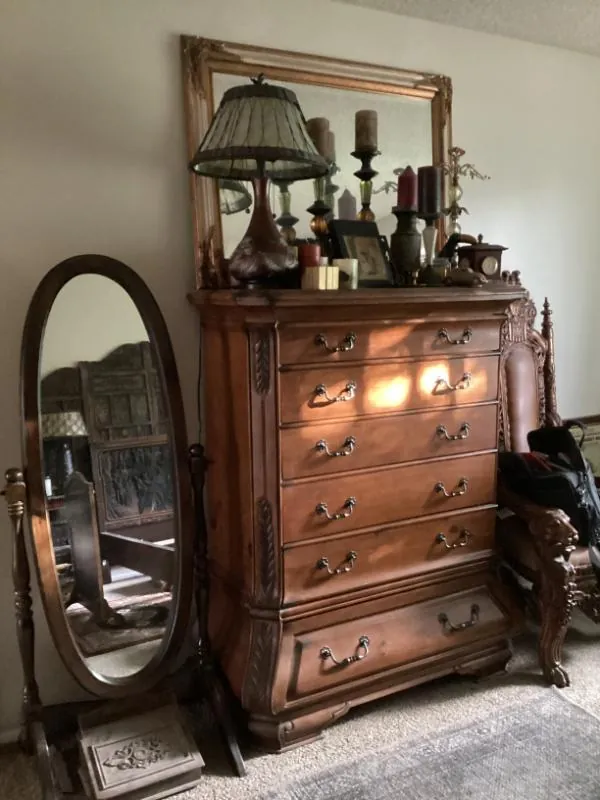Wood chest of drawers with a mirror, beside an oval standing mirror
