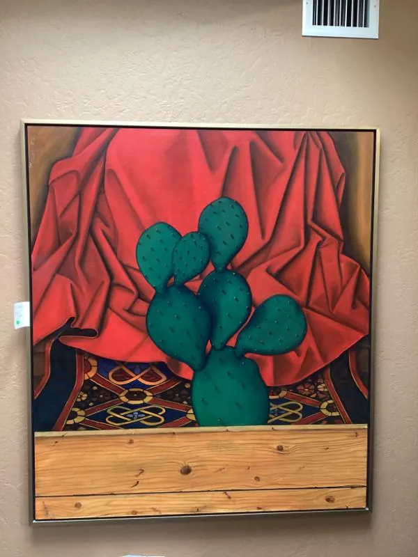 Painting of a prickly pear cactus in front of a red curtain