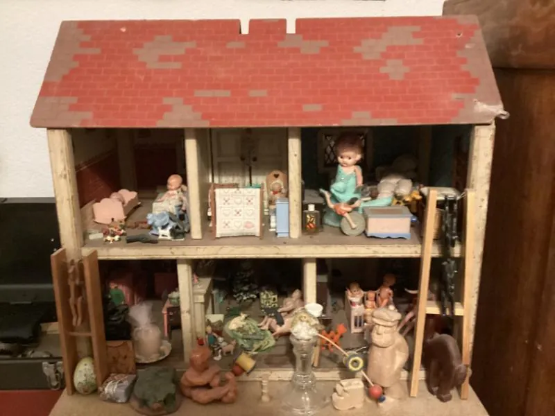 Old wooden dollhouse with a red roof, filled with tiny furniture