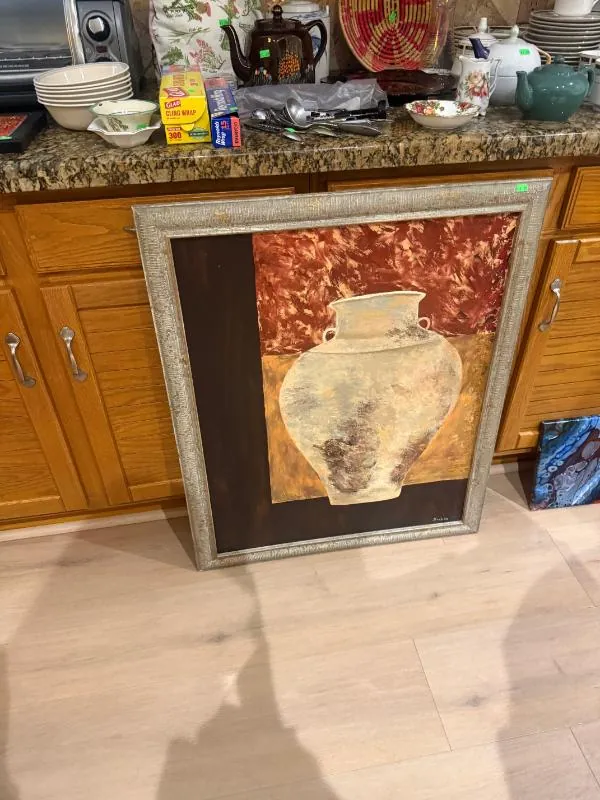 Framed painting of a vase, leaning against kitchen cabinets