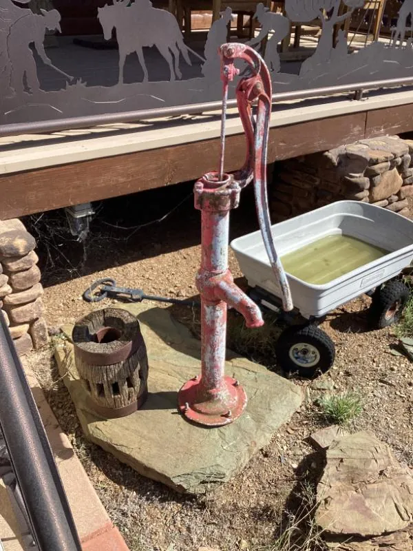 Red hand water pump next to a metal wagon