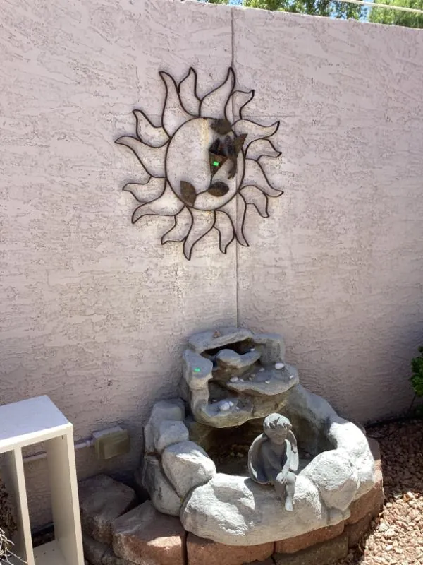 Sun-shaped metal wall art above a tiered fountain