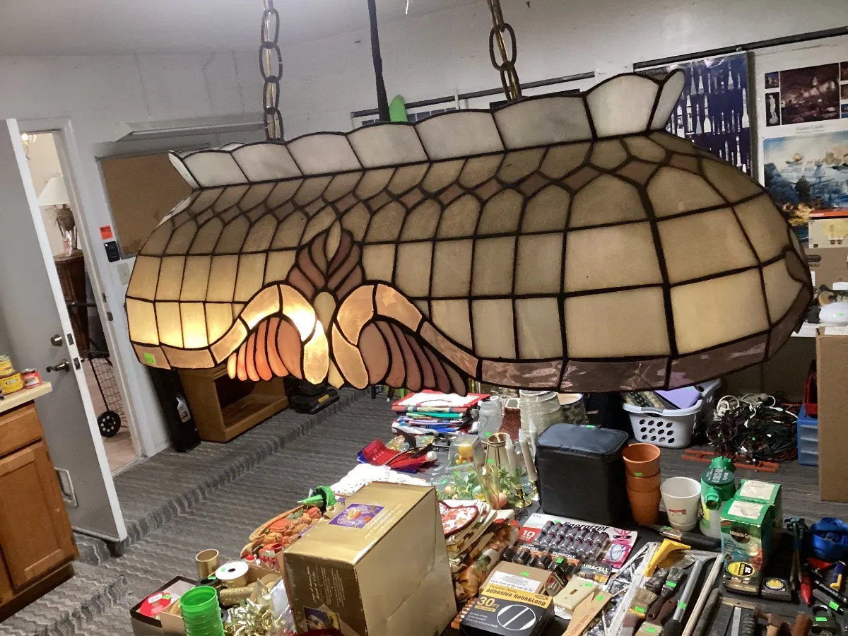 Stained-glass-style light hanging from chains, lit up above tables of sale items