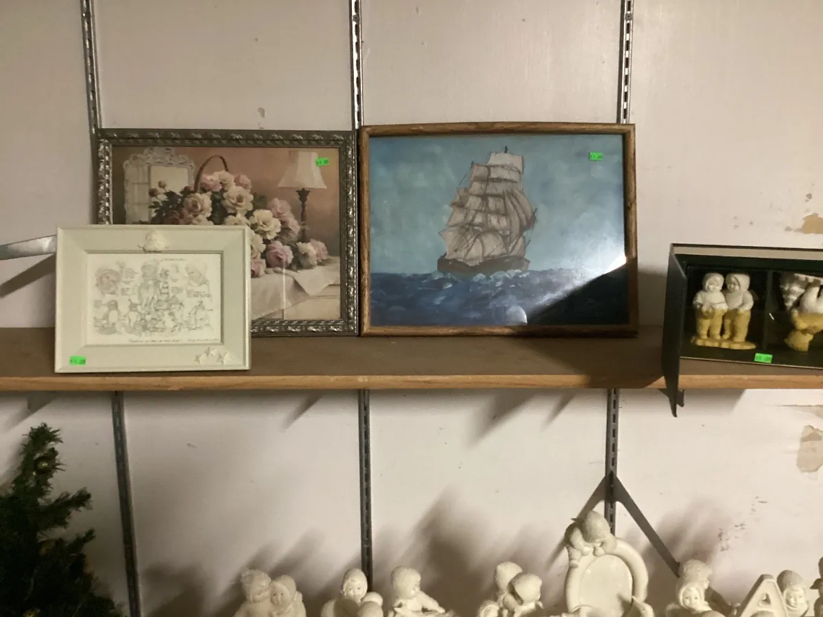 Framed artwork on a shelf, including a painting of a sailing ship