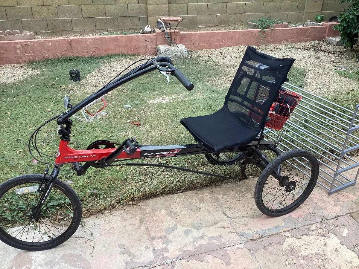 Red and black recumbent tricycle with a mesh seat, parked in a backyard