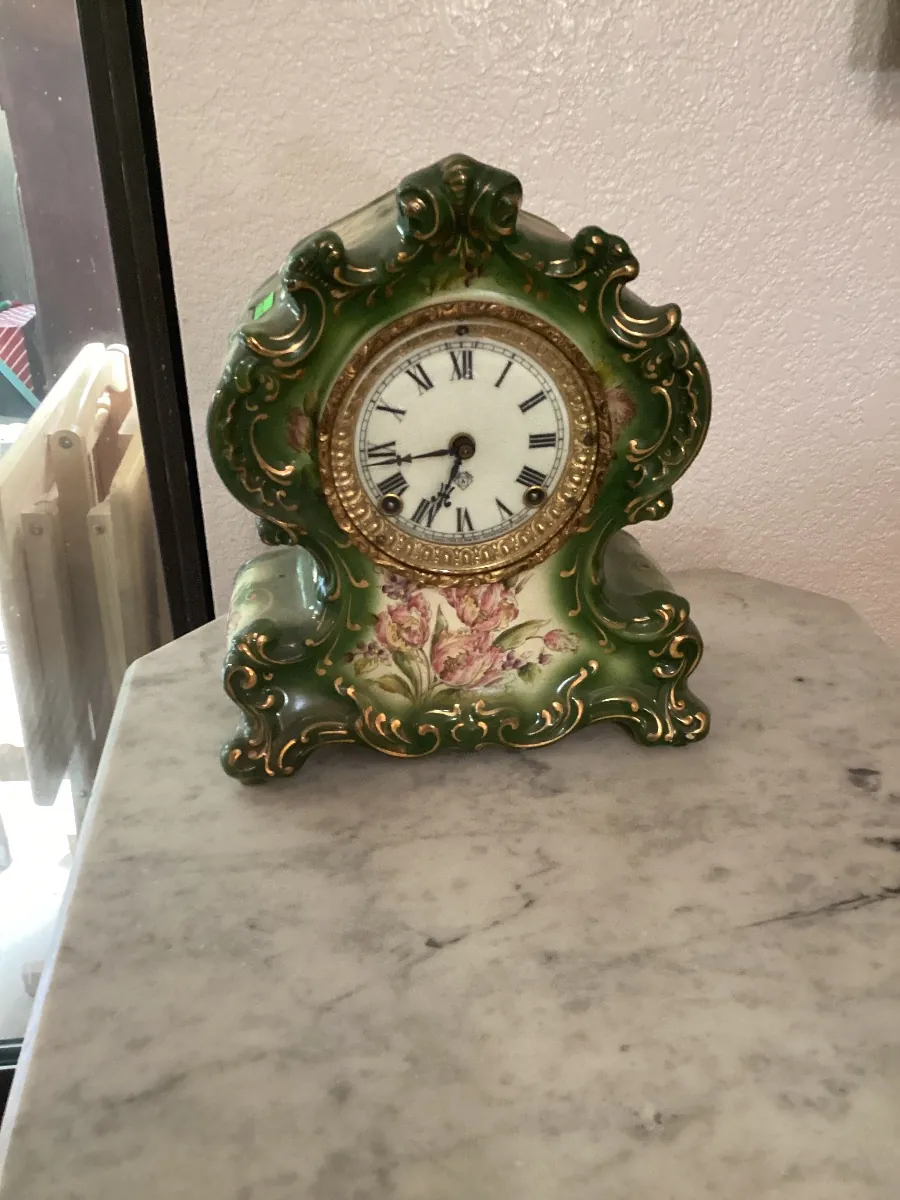 Green and gold mantel clock painted with roses, on a marble top